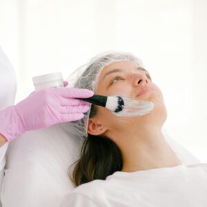A beautician applies a facial treatment cream on a woman in a clinic setting.