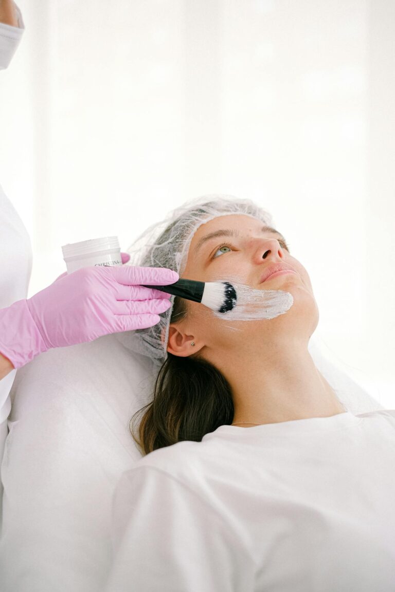 A beautician applies a facial treatment cream on a woman in a clinic setting.